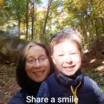 A woman and her young son smile at the camera in front of a tree-lined path. Words at the bottom say "Share a smile"