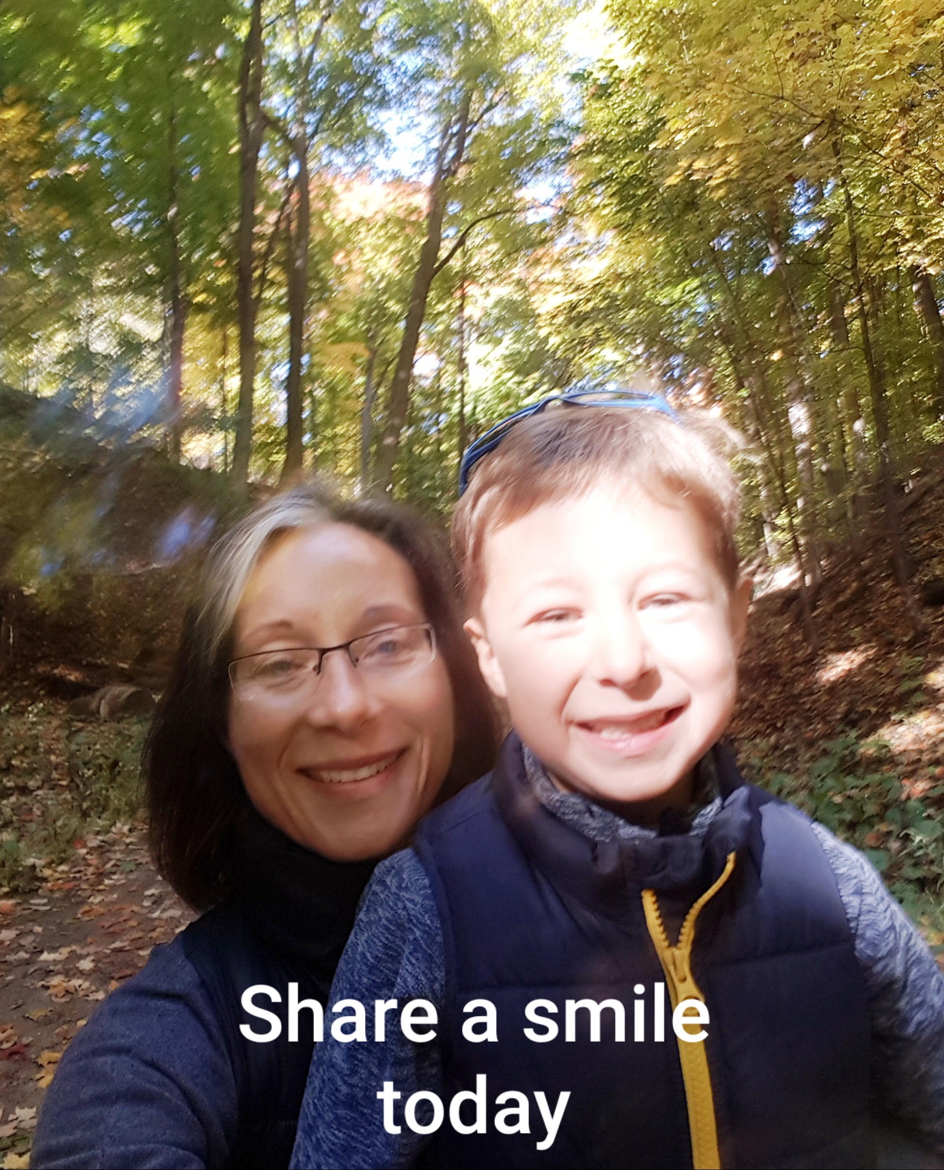 A woman and her young son smile at the camera in front of a tree-lined path. Words at the bottom say "Share a smile"