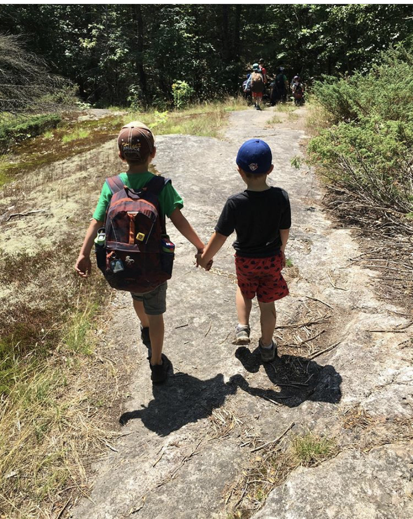 Two boys hold hands and walk down a dirt path in nature